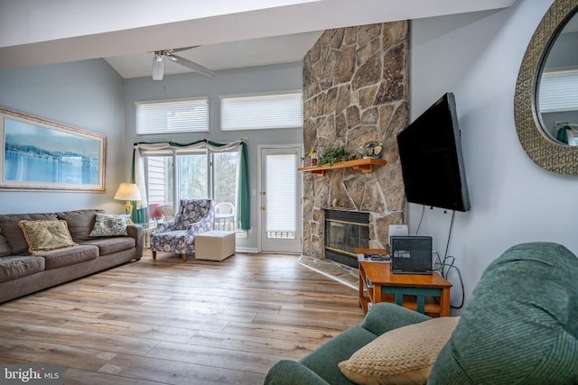 living room featuring a stone fireplace, light hardwood / wood-style flooring, ceiling fan, and a towering ceiling