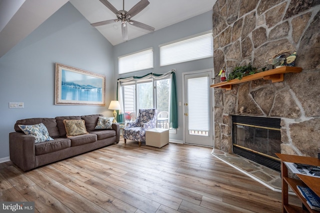 living room with wood-type flooring, a stone fireplace, ceiling fan, and high vaulted ceiling