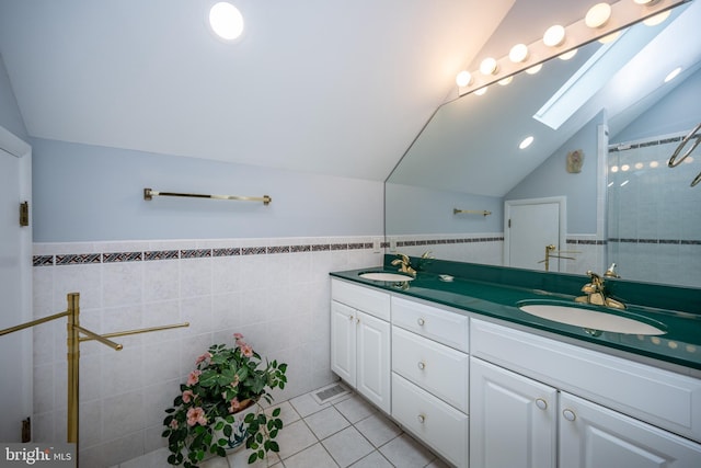 bathroom with walk in shower, lofted ceiling with skylight, tile walls, vanity, and tile patterned flooring