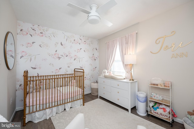 bedroom with a nursery area, ceiling fan, and wood-type flooring