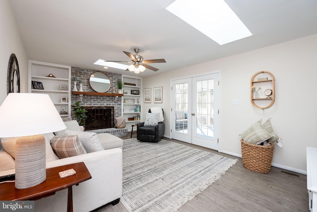 living room featuring french doors, built in shelves, a brick fireplace, and a skylight