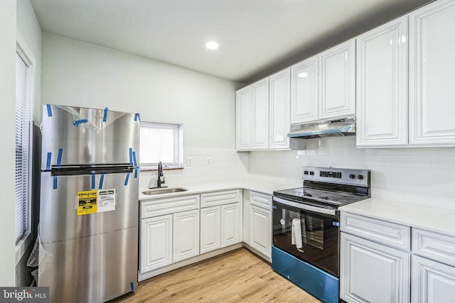 kitchen with appliances with stainless steel finishes, sink, white cabinets, backsplash, and light hardwood / wood-style floors