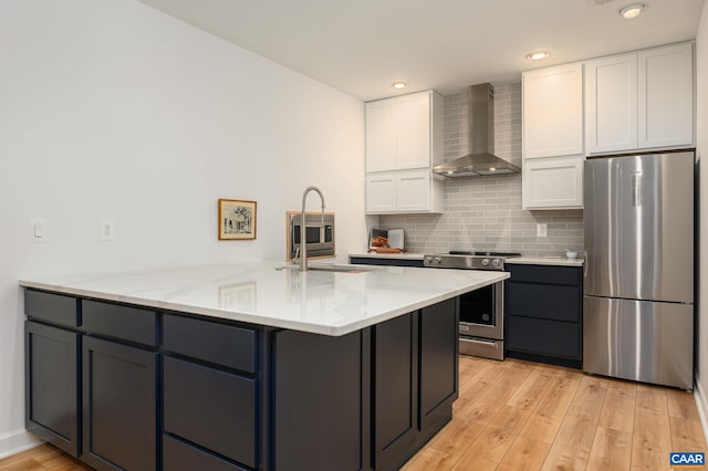 kitchen with sink, white cabinetry, stainless steel appliances, light stone countertops, and wall chimney range hood