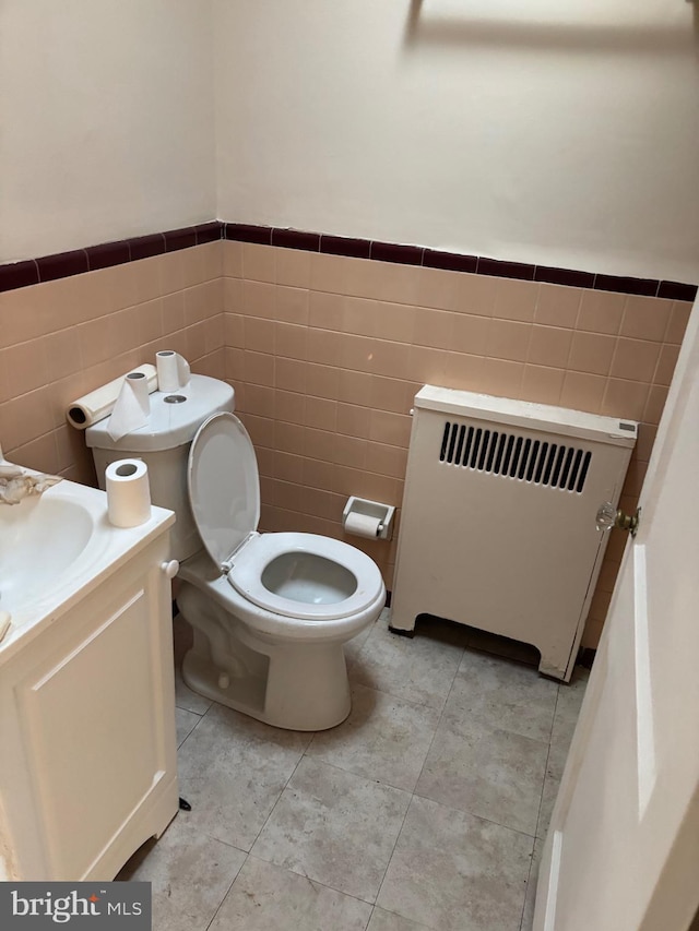 bathroom featuring tile walls, radiator heating unit, vanity, tile patterned floors, and toilet