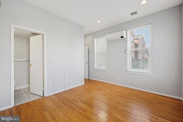 unfurnished bedroom with a wall mounted air conditioner and light hardwood / wood-style floors