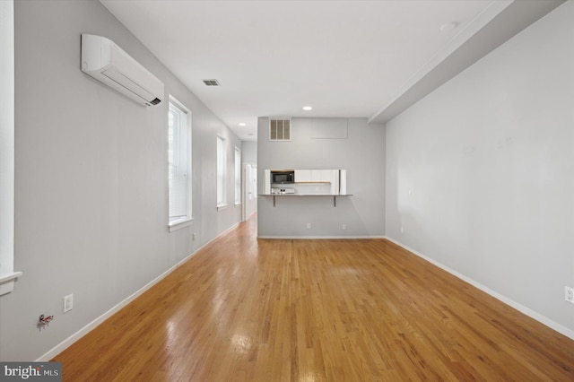 unfurnished living room with an AC wall unit and light wood-type flooring