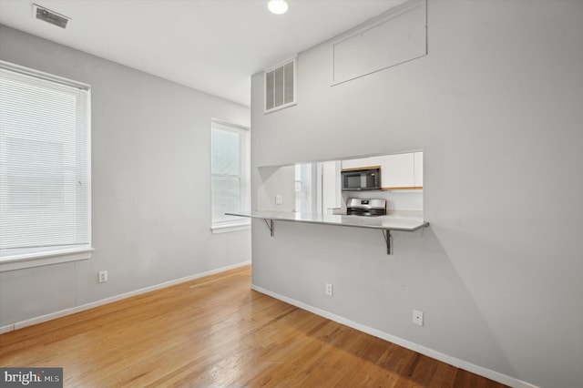 kitchen with stainless steel stove, white cabinets, a kitchen bar, light hardwood / wood-style floors, and kitchen peninsula