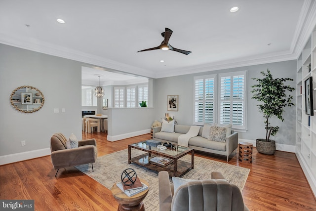 living room with ornamental molding, ceiling fan with notable chandelier, and light hardwood / wood-style flooring