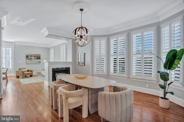 dining room with crown molding, light wood-type flooring, an inviting chandelier, and a fireplace