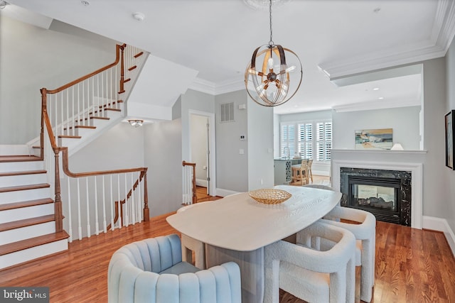 dining room with a premium fireplace, ornamental molding, an inviting chandelier, and light hardwood / wood-style flooring