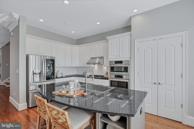 kitchen featuring a kitchen bar, white cabinetry, dark stone counters, stainless steel appliances, and a kitchen island with sink