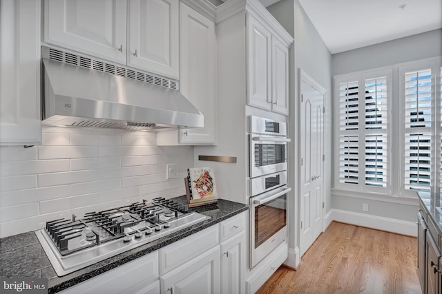 kitchen with white cabinets, dark stone counters, decorative backsplash, stainless steel appliances, and light wood-type flooring