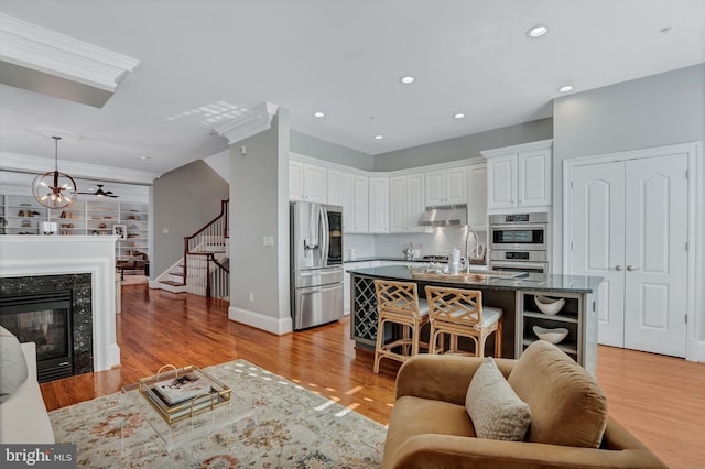 living room with sink, an inviting chandelier, a fireplace, ornamental molding, and light wood-type flooring