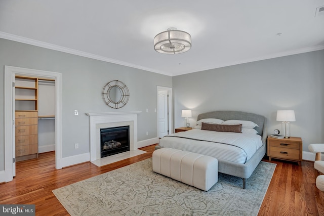 bedroom featuring hardwood / wood-style flooring, a walk in closet, and ornamental molding