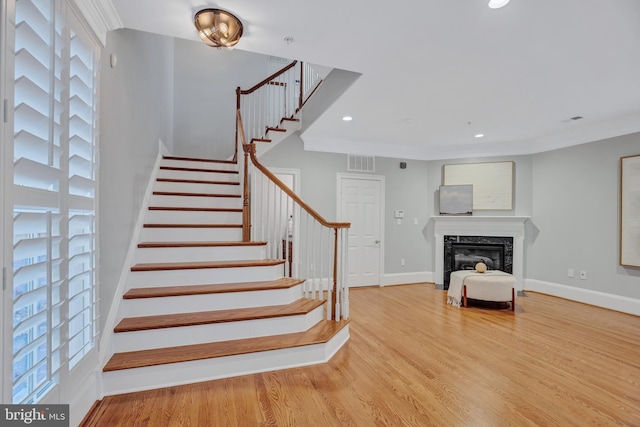 stairs with a premium fireplace, crown molding, and hardwood / wood-style floors