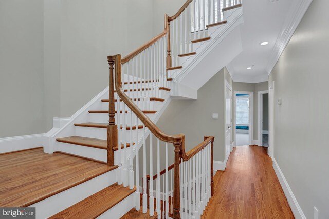 stairway with ornamental molding and hardwood / wood-style floors