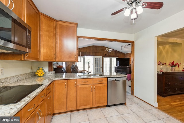 kitchen with brown cabinetry, light stone countertops, a peninsula, a sink, and stainless steel appliances