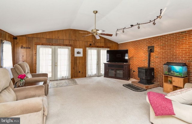 carpeted living room with lofted ceiling, a wood stove, wooden walls, and french doors