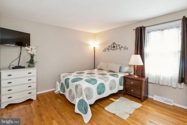 bedroom featuring light wood-style floors, visible vents, and baseboards