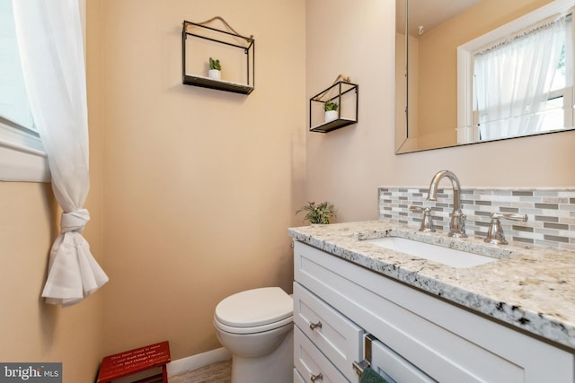 half bathroom featuring vanity, toilet, baseboards, and backsplash