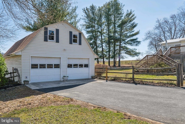 view of home's exterior featuring a gambrel roof, an outbuilding, a detached garage, and fence