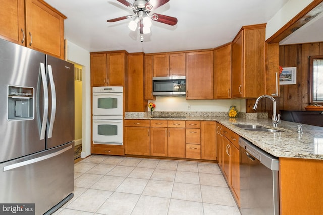 kitchen featuring brown cabinetry, light stone countertops, light tile patterned flooring, a sink, and stainless steel appliances