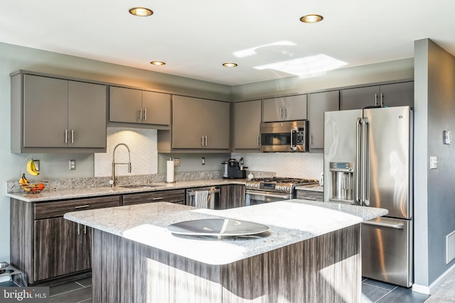 kitchen with sink, tasteful backsplash, a kitchen island, stainless steel appliances, and light stone countertops