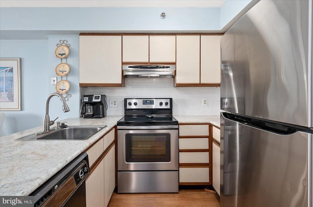 kitchen with under cabinet range hood, stainless steel appliances, a sink, light wood-type flooring, and backsplash