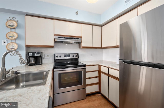 kitchen with appliances with stainless steel finishes, tasteful backsplash, sink, white cabinets, and light wood-type flooring