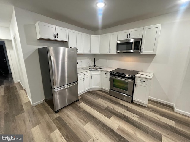 kitchen with stainless steel appliances, white cabinets, light countertops, and wood finished floors