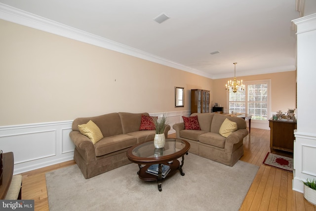 living room with an inviting chandelier, ornamental molding, and light hardwood / wood-style floors