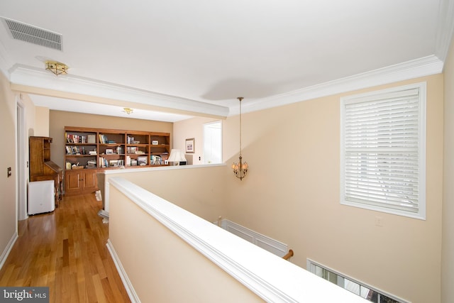 hall featuring ornamental molding, light hardwood / wood-style floors, and a notable chandelier