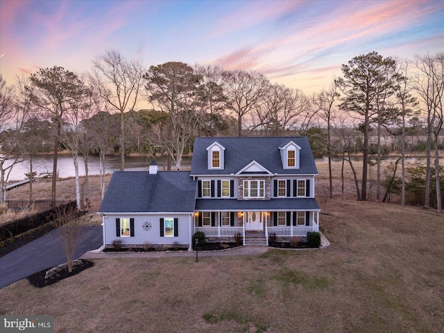 colonial-style house with a yard, a water view, and a porch