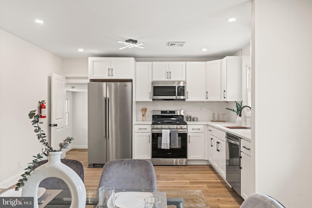 kitchen with sink, white cabinetry, stainless steel appliances, tasteful backsplash, and light wood-type flooring