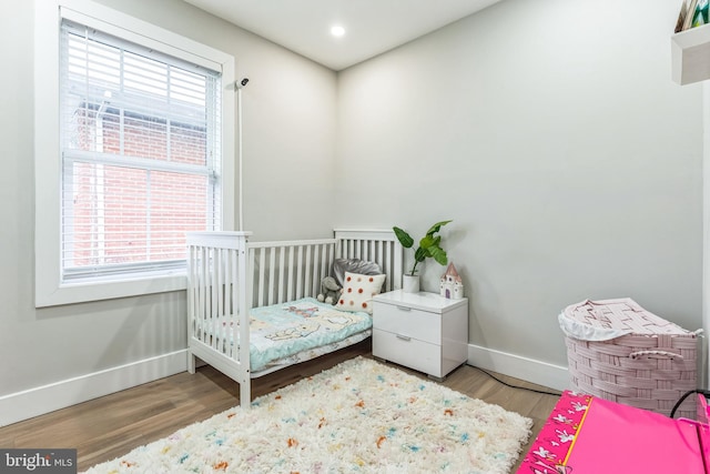 bedroom with multiple windows, wood-type flooring, and a nursery area