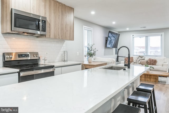 kitchen featuring a breakfast bar, sink, hardwood / wood-style flooring, stainless steel appliances, and backsplash