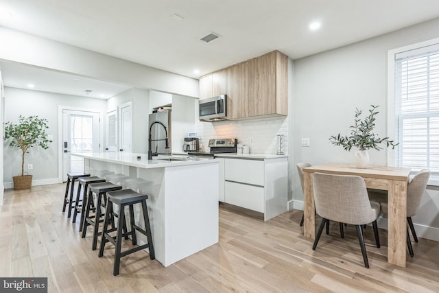 kitchen featuring appliances with stainless steel finishes, white cabinets, decorative backsplash, a center island with sink, and light wood-type flooring