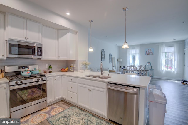 kitchen featuring appliances with stainless steel finishes, pendant lighting, sink, white cabinets, and kitchen peninsula