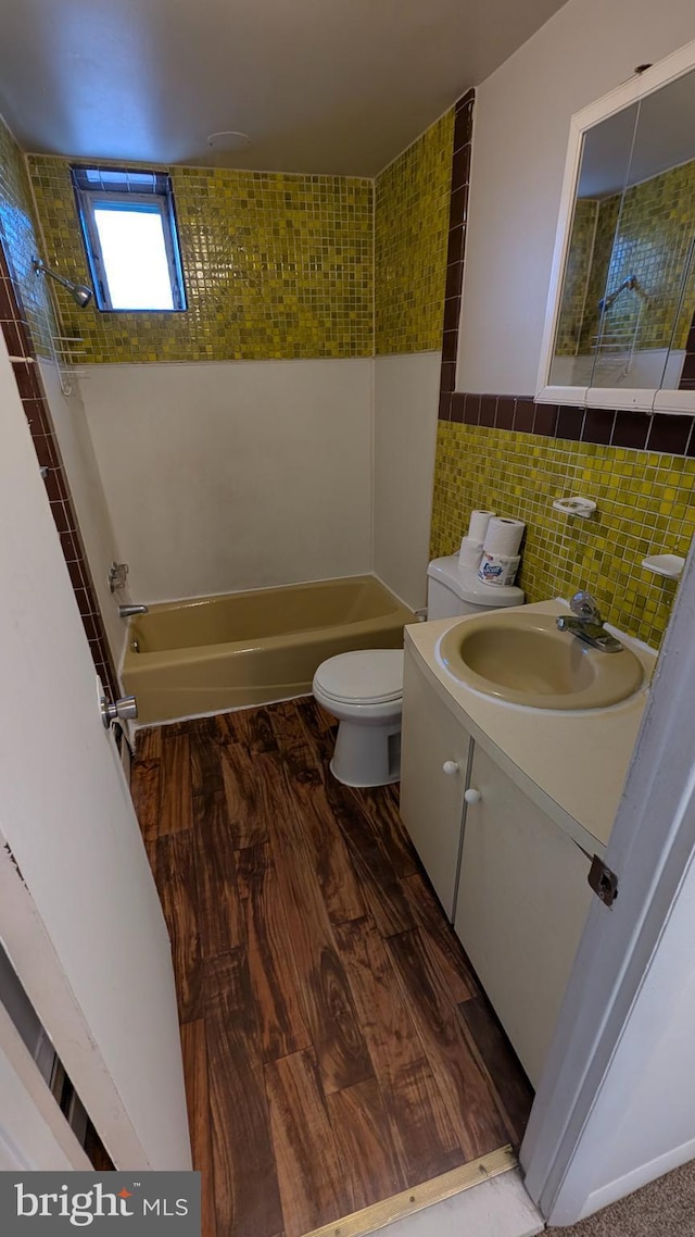 full bathroom with hardwood / wood-style flooring, tile walls, vanity, toilet, and tiled shower / bath