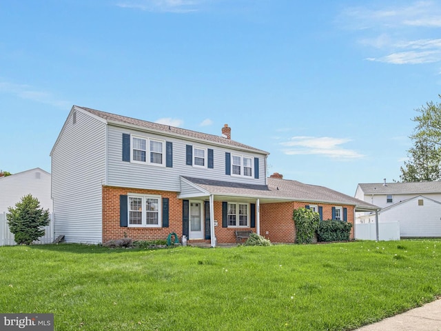 view of front facade featuring a chimney, covered porch, fence, brick siding, and a front lawn