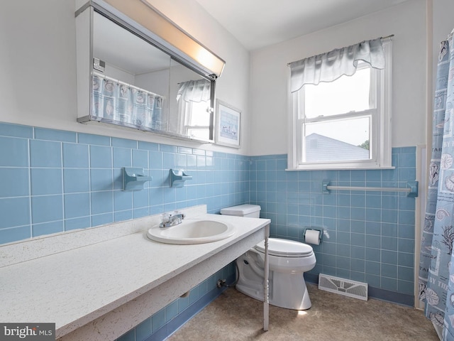 full bathroom featuring tile walls, a wainscoted wall, toilet, a sink, and visible vents