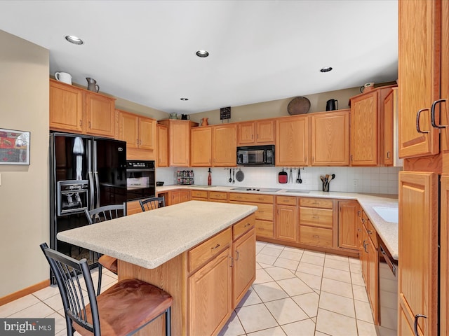 kitchen featuring light tile patterned floors, backsplash, a center island, black appliances, and a kitchen bar