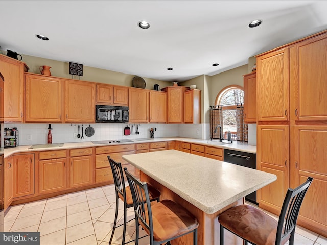 kitchen with light tile patterned flooring, tasteful backsplash, sink, a kitchen breakfast bar, and black appliances