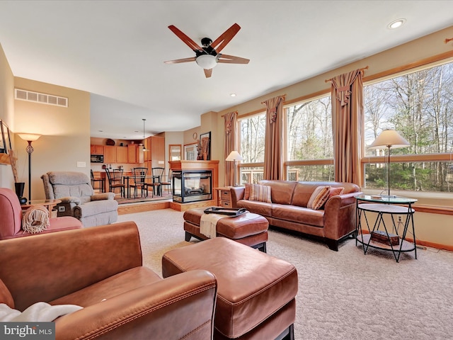 carpeted living room featuring ceiling fan, a multi sided fireplace, and plenty of natural light