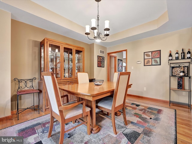 dining room featuring light hardwood / wood-style flooring, an inviting chandelier, and a tray ceiling