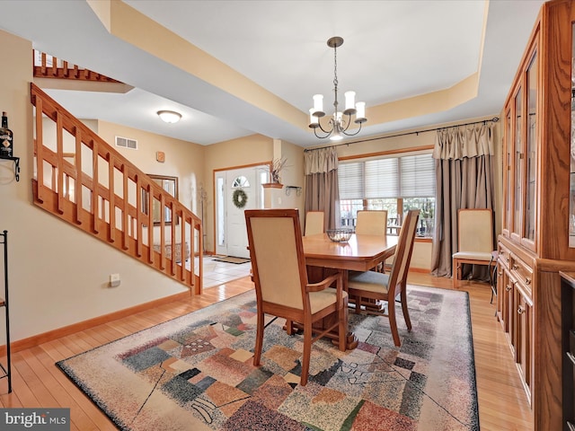 dining room featuring an inviting chandelier, a tray ceiling, and light hardwood / wood-style flooring