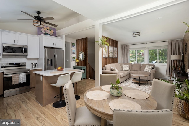 dining space featuring ceiling fan, vaulted ceiling, and light hardwood / wood-style flooring