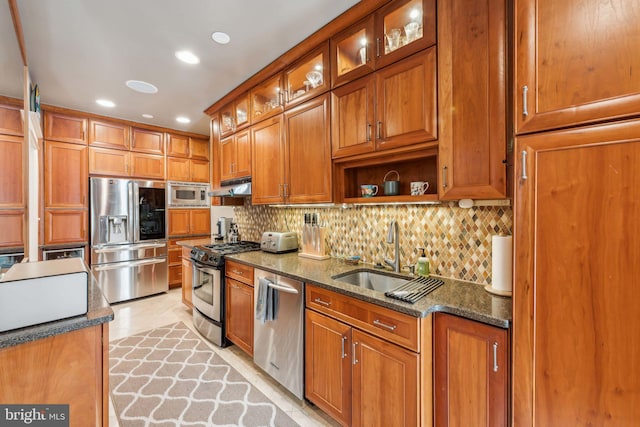 kitchen featuring sink, dark stone countertops, backsplash, stainless steel appliances, and light tile patterned flooring