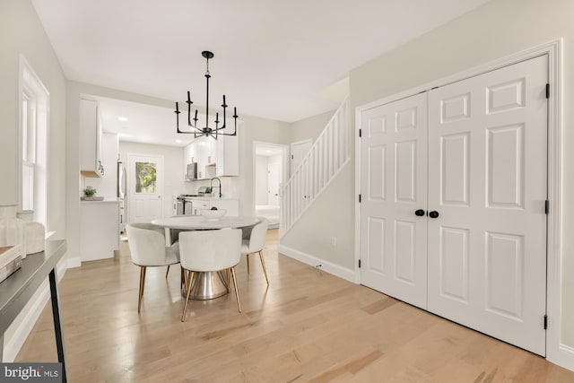 dining space with an inviting chandelier, baseboards, light wood finished floors, and stairs