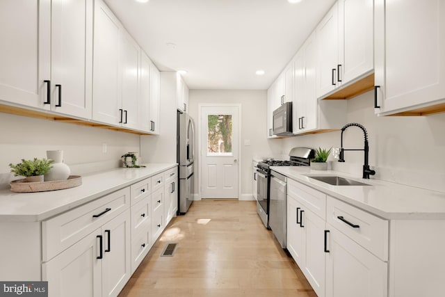 kitchen with stainless steel appliances, a sink, visible vents, white cabinetry, and light countertops